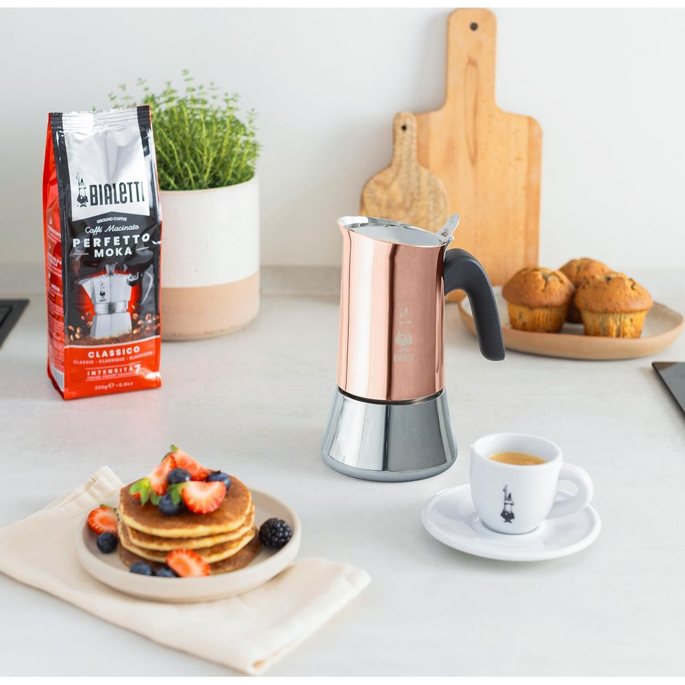 Miedziany ekspres do kawy z kawą, babeczkami i naleśnikami na blacie.