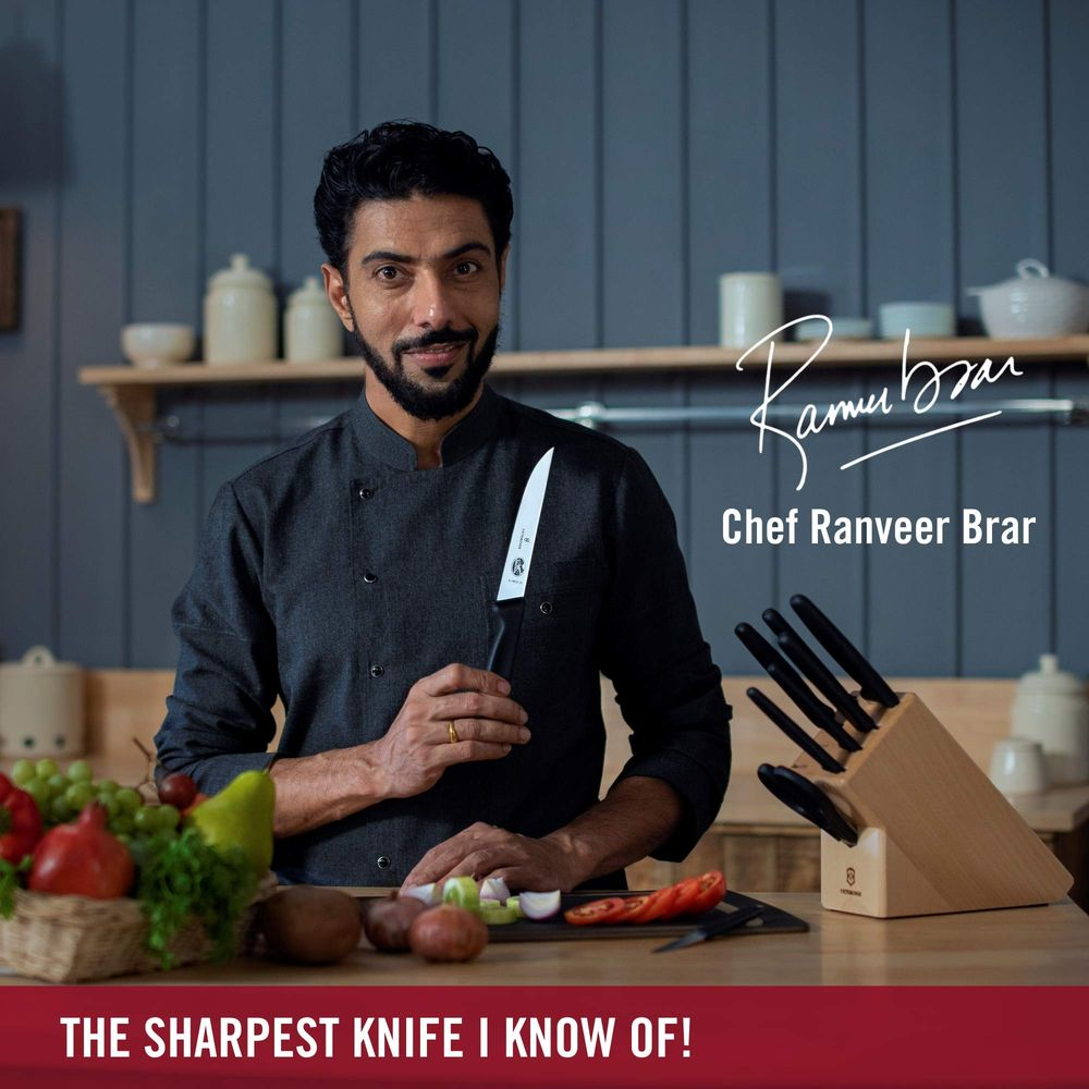 Koch Ranveer Brar hält ein Messer. Daneben ein Holzblock mit Messern und Obst.