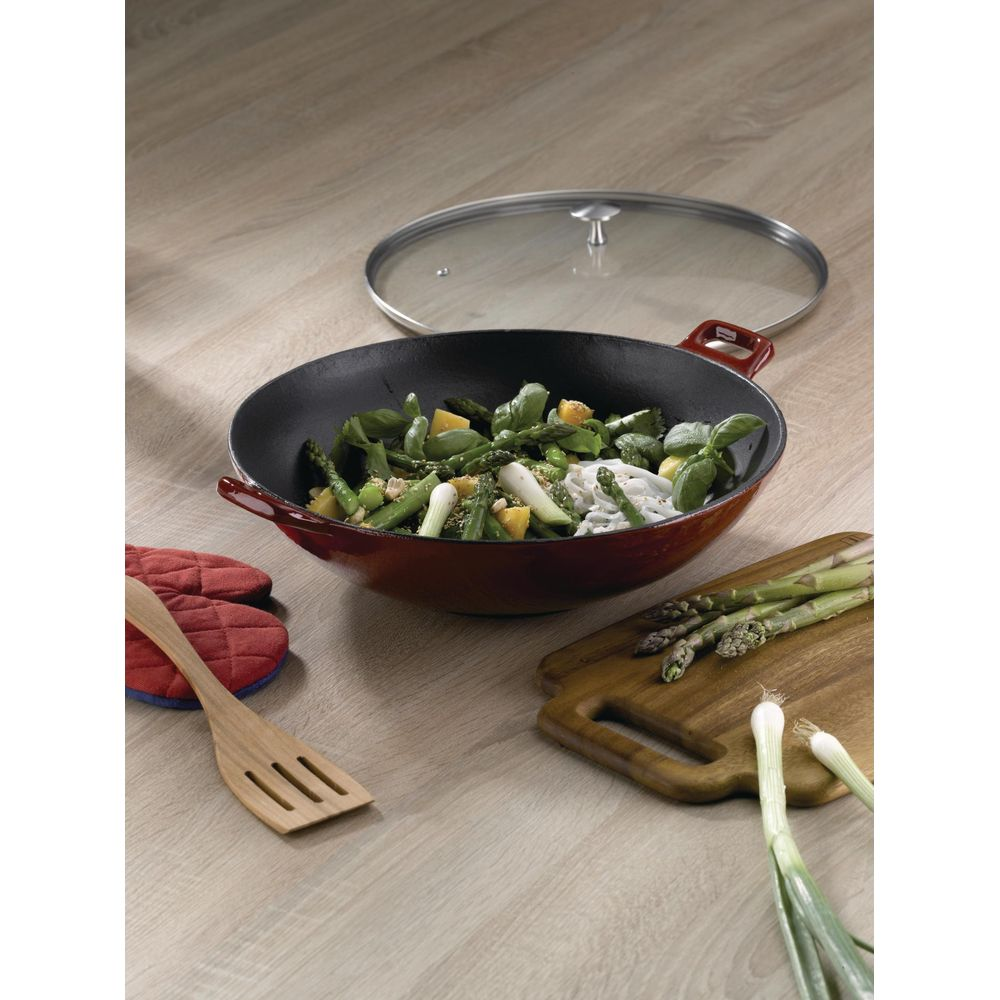Ein roter Wok mit Gemüse und Nudeln, daneben ein Schneidebrett mit Spargel.