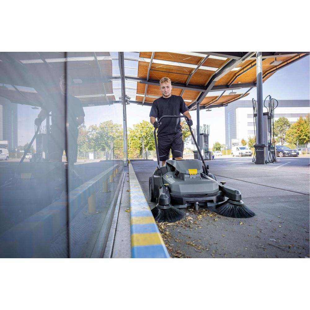 Mann mit Kehrmaschine reinigt Gehweg mit Laub.