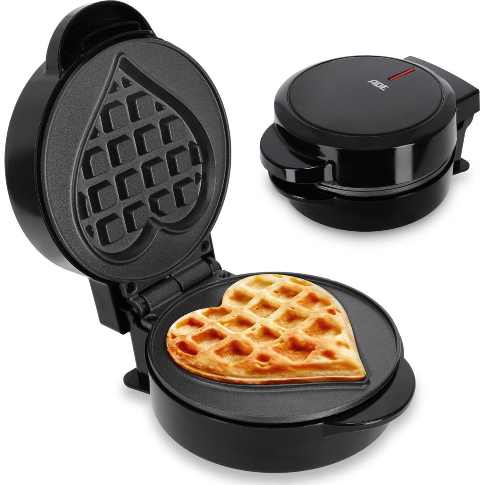 Otwarta czarna gofrownica w kształcie serca z złotym gofrem w środku. Druga gofrownica jest zamknięta.