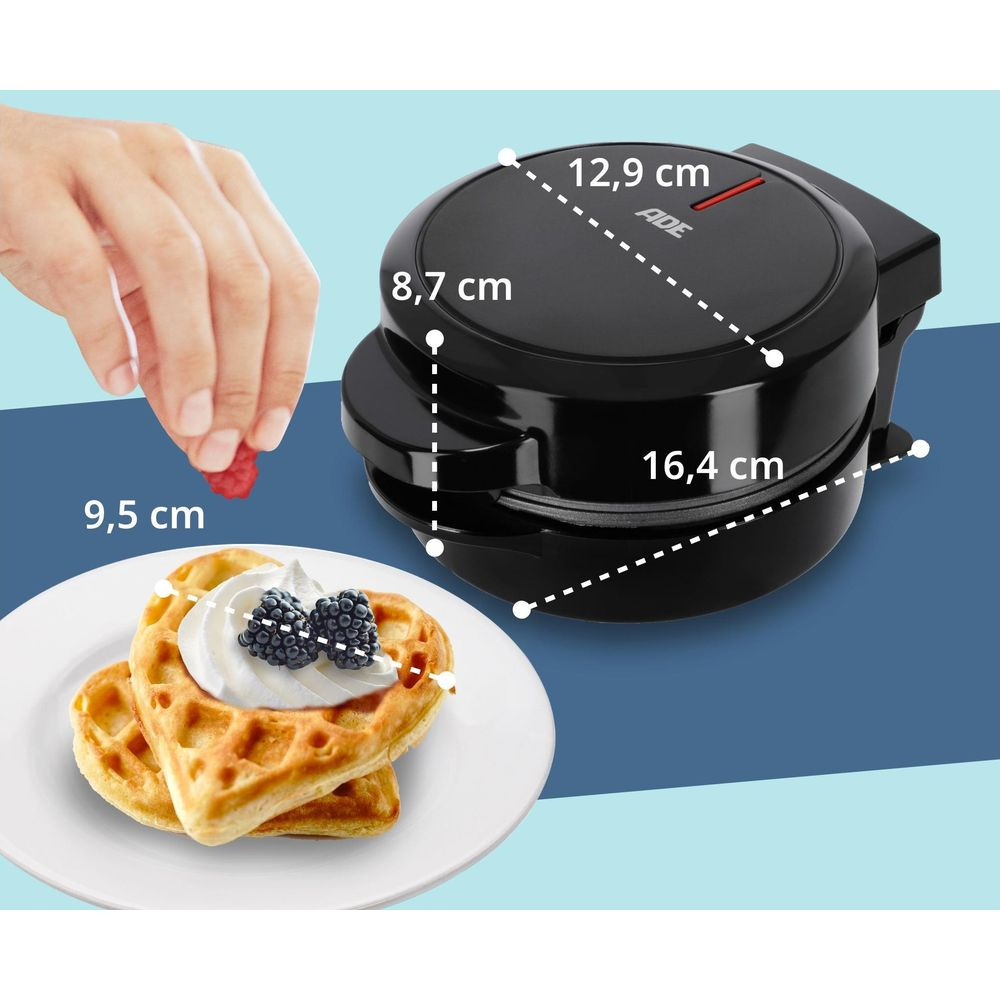 Mężczyzna trzyma malinę obok gofrownicy i wafli w kształcie serca.