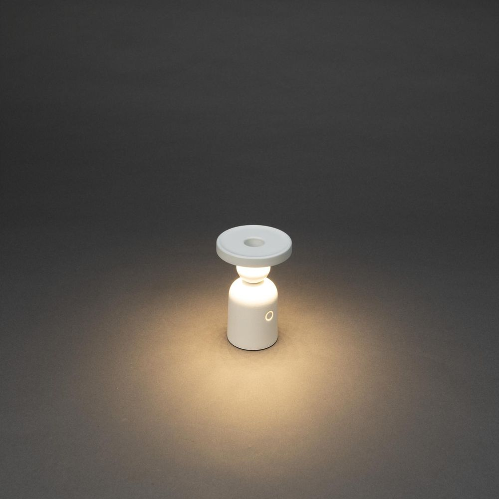 Eine weiße, zylindrische Lampe mit einem runden oberen Aufsatz, die auf einem dunklen Hintergrund leuchtet.