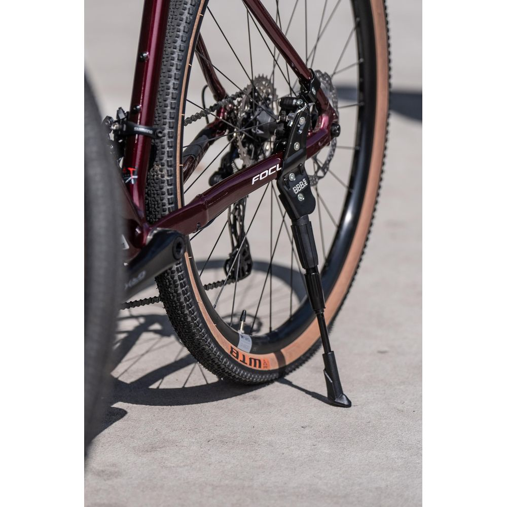 Zbliżenie tylnego koła ciemnoczerwonego roweru z podpórką.