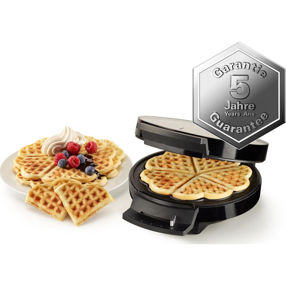 Ein Waffeleisen mit fertigen Waffeln, garniert mit Sahne und Beeren.