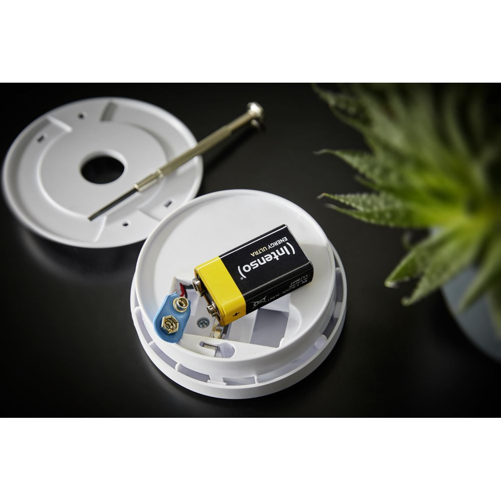 Bateria 9V jest wkładana do białego czujnika dymu. Obok leży mały śrubokręt.