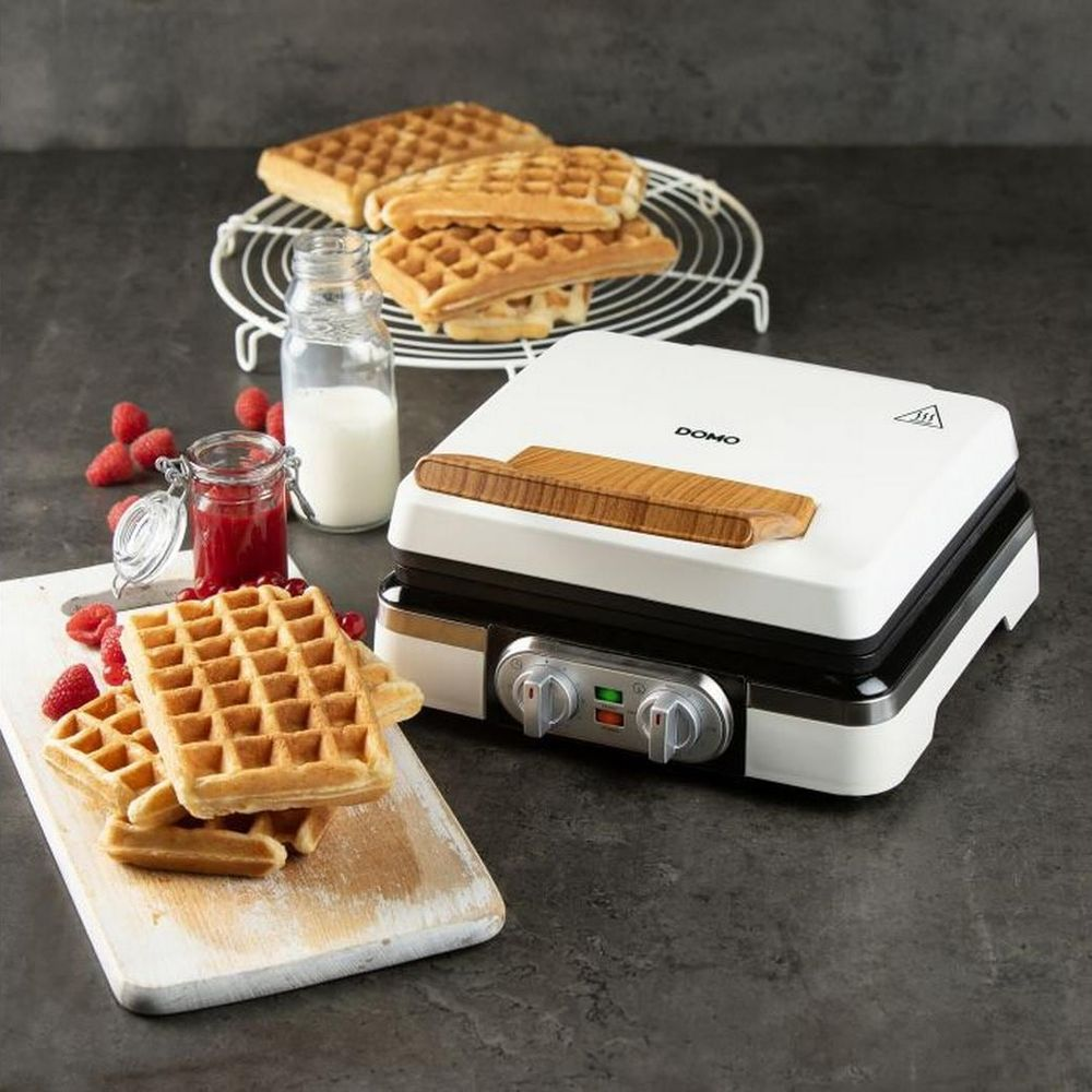 Una piastra per waffle bianca con manico in legno, accanto a waffle, bacche e marmellata.
