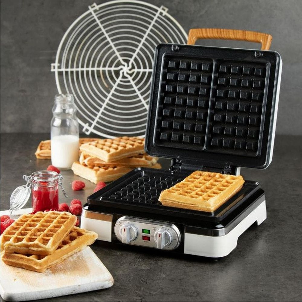 Una piastra per waffle con waffle finiti, lamponi, marmellata e latte.