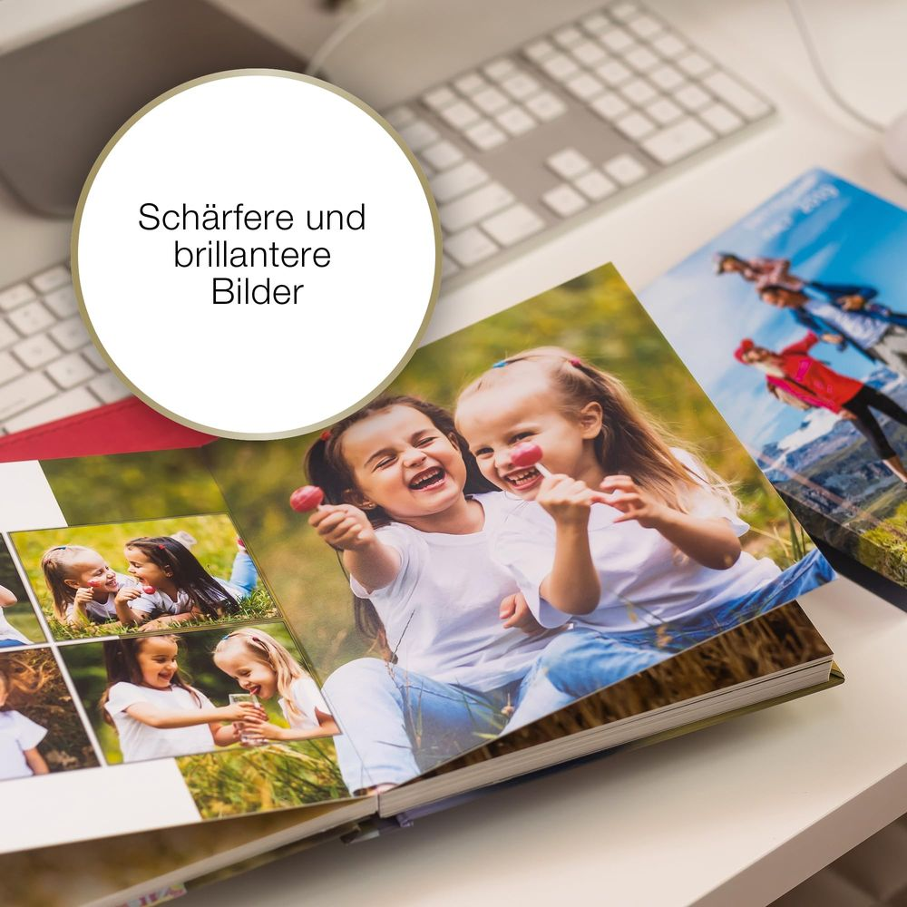 Dwie śmiejące się dziewczynki z lizakami przed fotoksiążką na biurku.