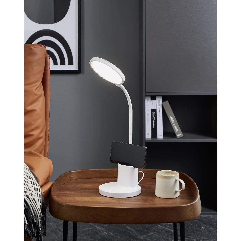 Une lampe de bureau blanche avec support de téléphone est sur une table en bois à côté d'une tasse.