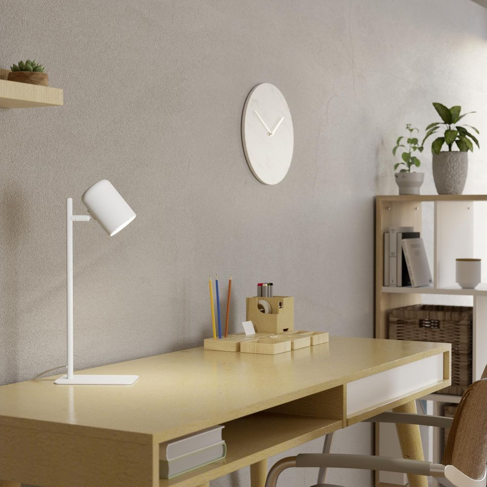 Ein weißer Schreibtisch mit Lampe, Stiften und Uhr an der Wand.