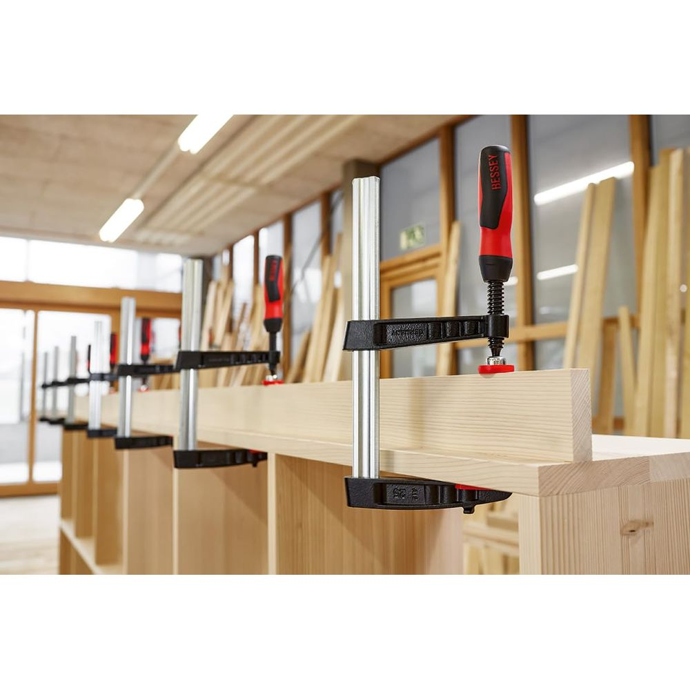 Mehrere Holzklemmen sichern ein Holzbrett auf einem Regal in einer Werkstatt.
