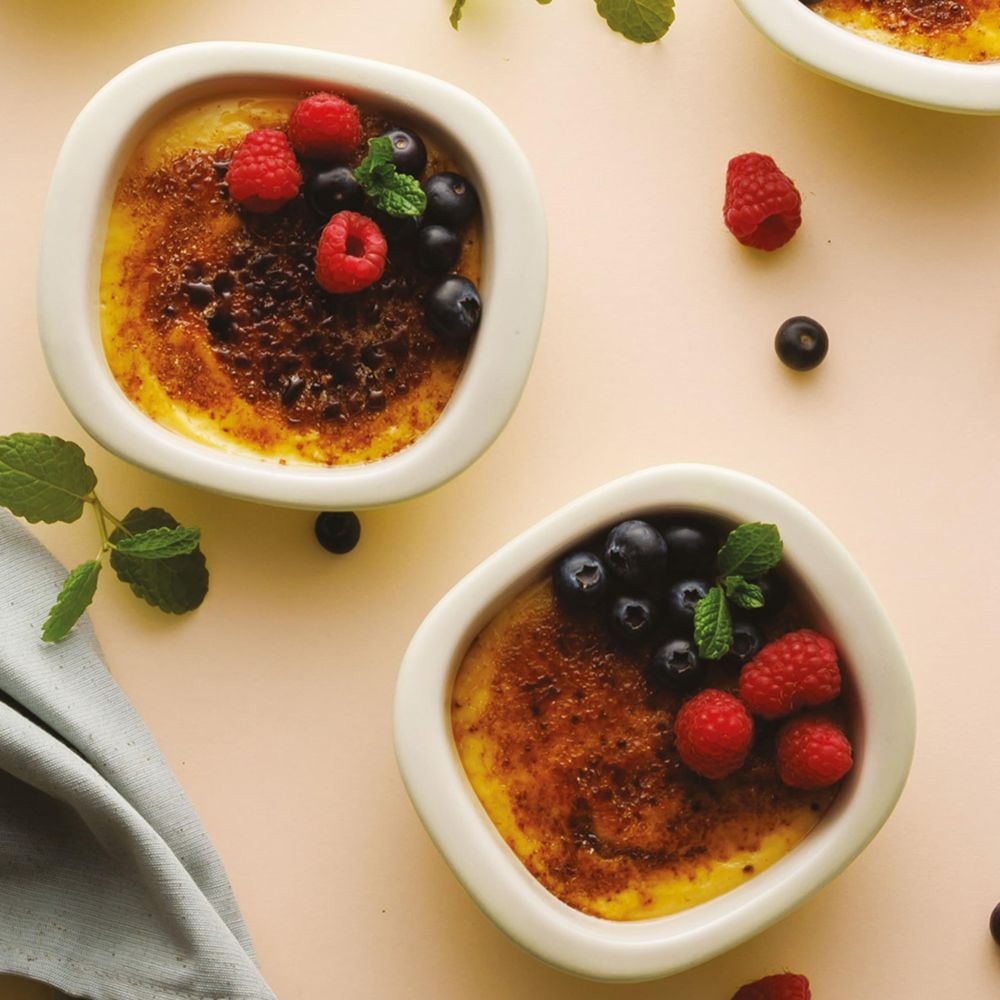 Dwa desery crème brûlée z malinami, jagodami i miętą.