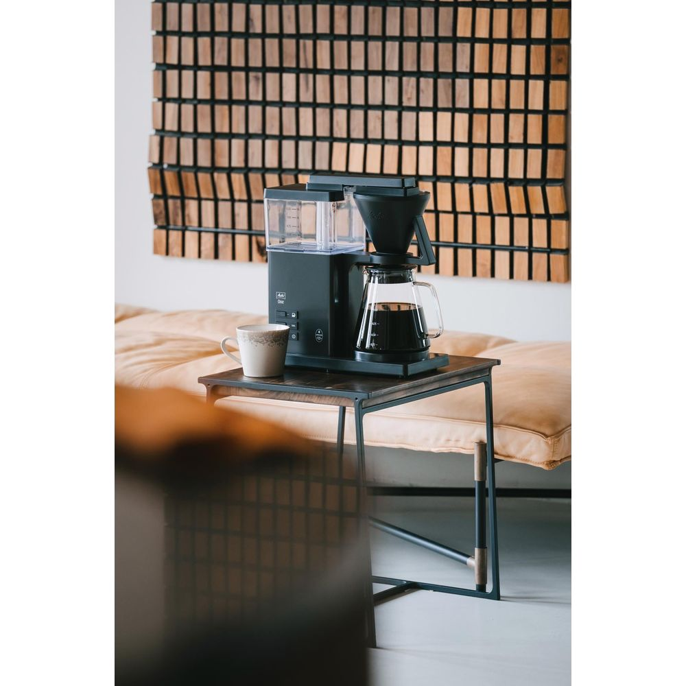 Czarny ekspres do kawy z szklanym dzbankiem i kubkiem na stole.