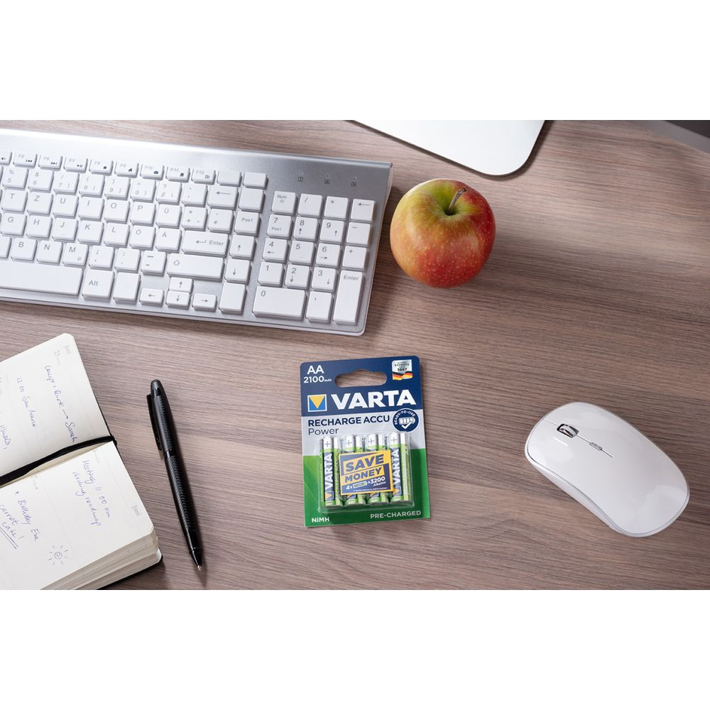 Ein Schreibtisch mit Tastatur, Maus, Notizbuch, Stift, Apfel und Batterien.