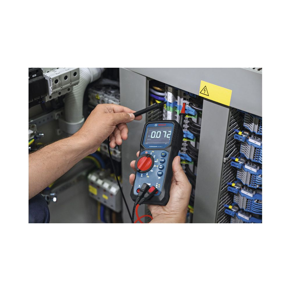 Hände mit Multimeter an elektrischer Schalttafel mit Kabeln.