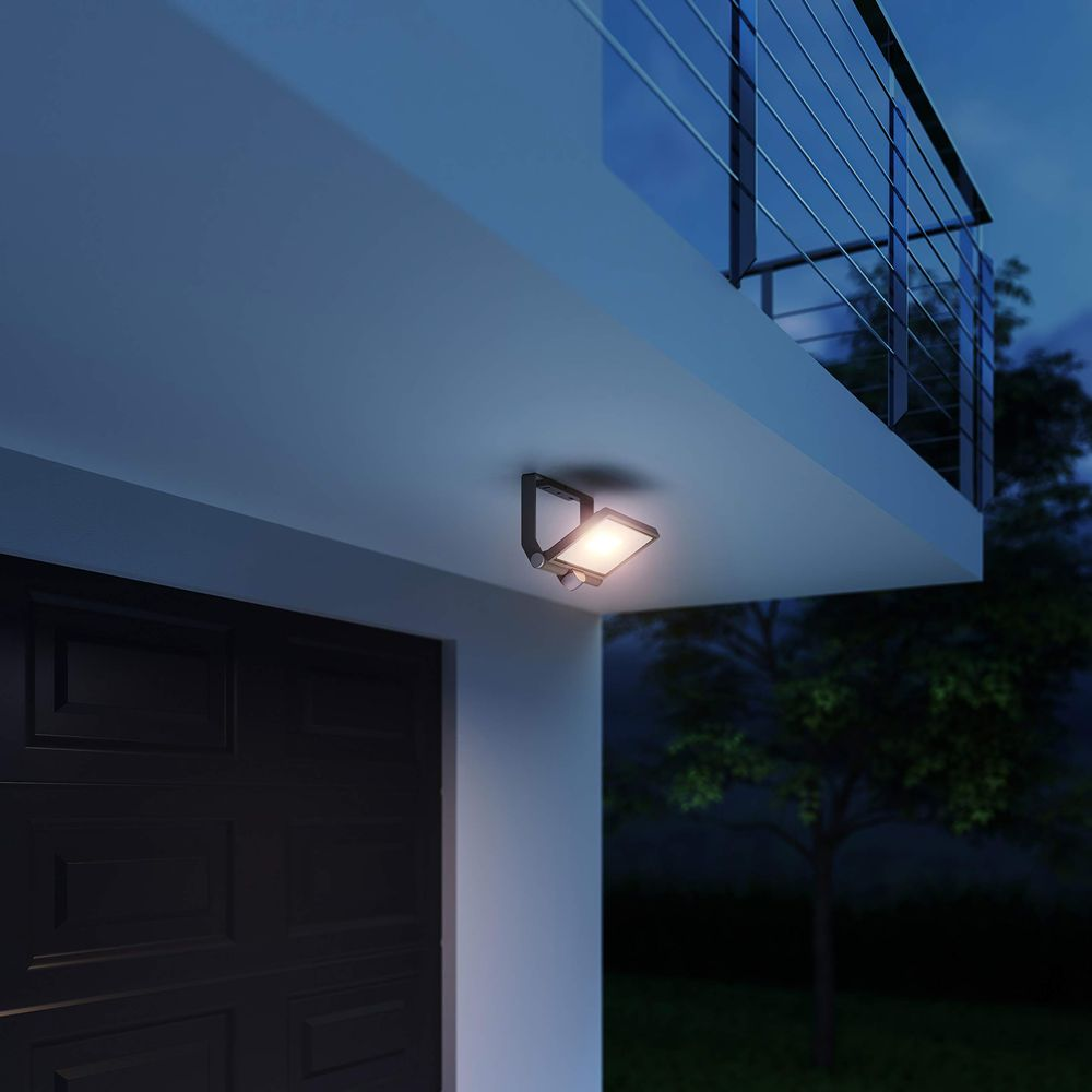 Ein moderner LED-Außenstrahler beleuchtet nachts eine Garagentür und einen Balkon.