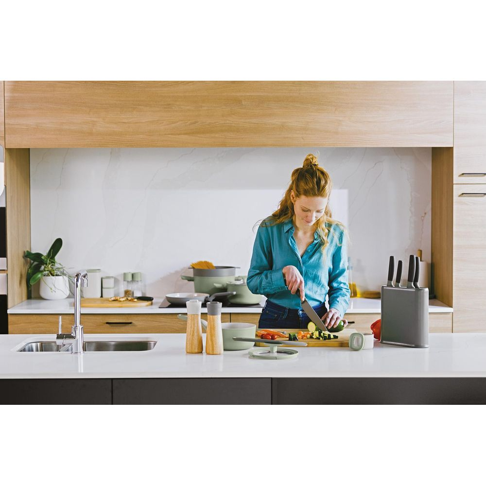 A woman in a blue shirt cuts vegetables in a modern kitchen.