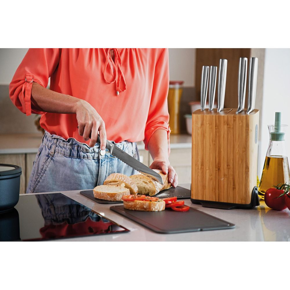 A person in an orange shirt slices bread in a kitchen with a knife block.