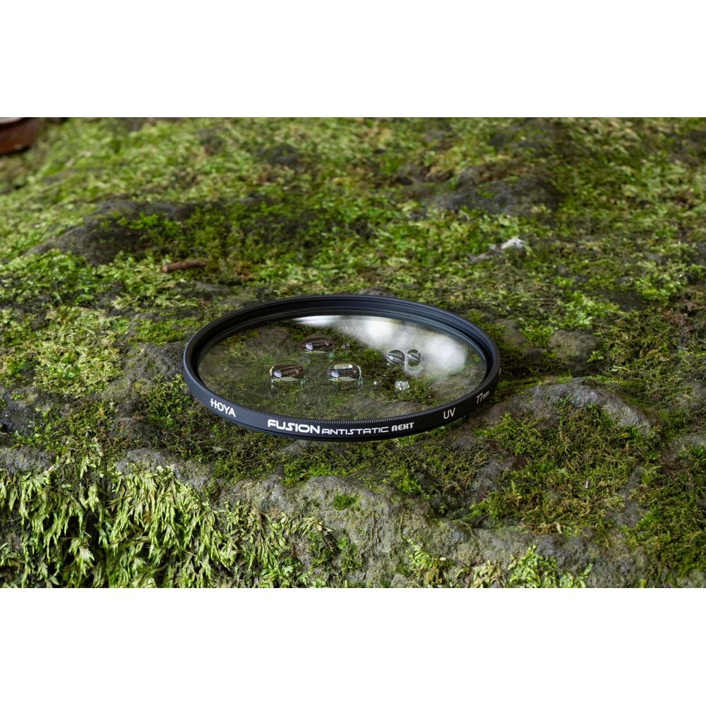 Ein Hoya UV-Filter mit Wassertropfen liegt auf moosbewachsenem Fels.