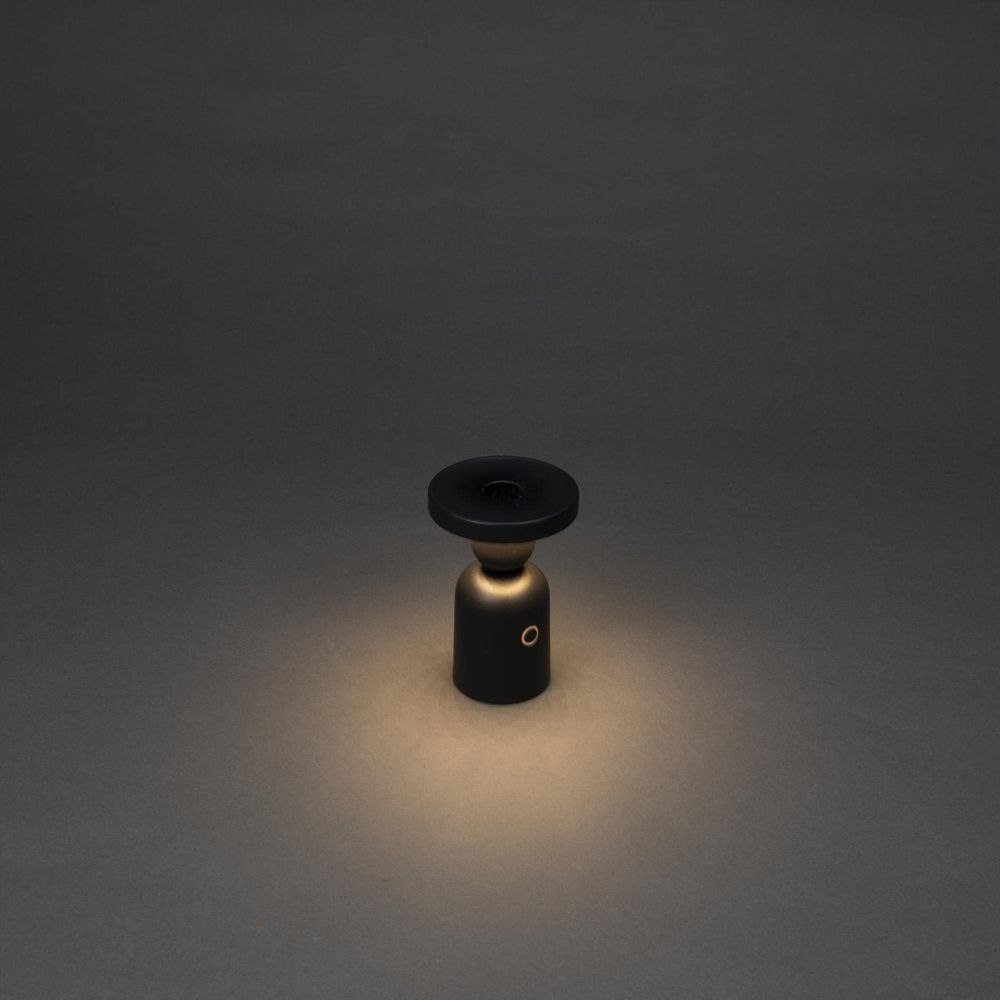Eine kleine schwarze Tischlampe mit einem kreisförmigen Lampenschirm steht auf einem dunklen Hintergrund.