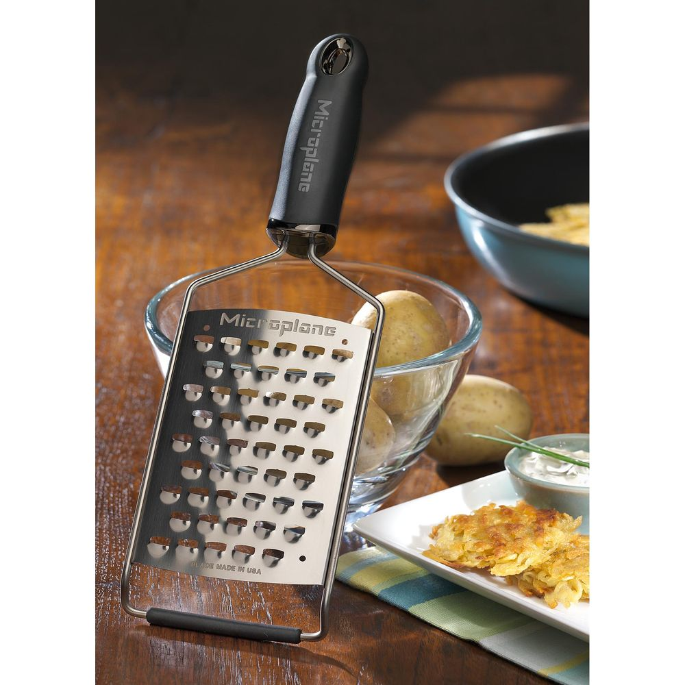 Ein Microplane-Raspel mit schwarzem Griff steht neben Kartoffeln in einer Schüssel.
