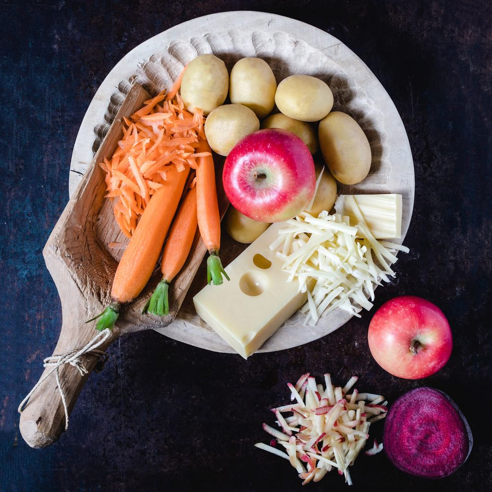 Rohe Kartoffeln, Karotten, Äpfel und Käse liegen auf einem Holzteller.