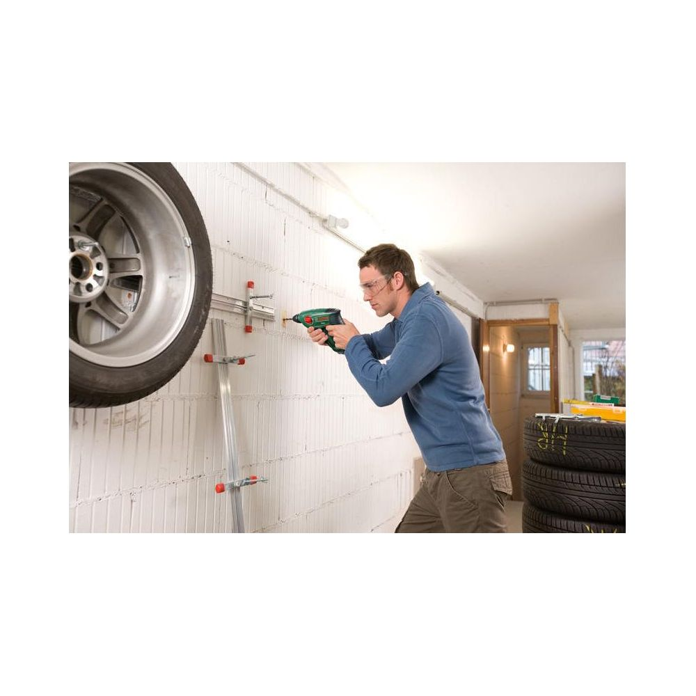 Mężczyzna wierci w białą ścianę; po lewej koło, po prawej stos opon.