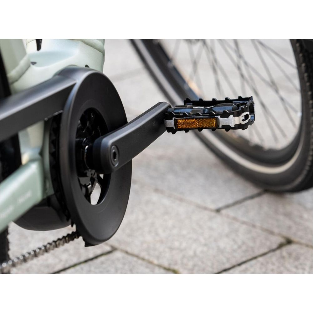 Zbliżenie korby roweru, pedału z odblaskiem i części tylnego koła.