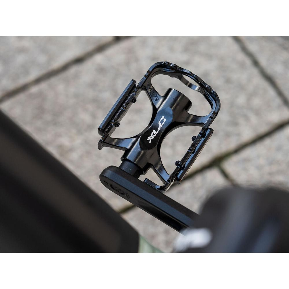 Czarny pedał rowerowy z logo XLC, na brukowanym tle.
