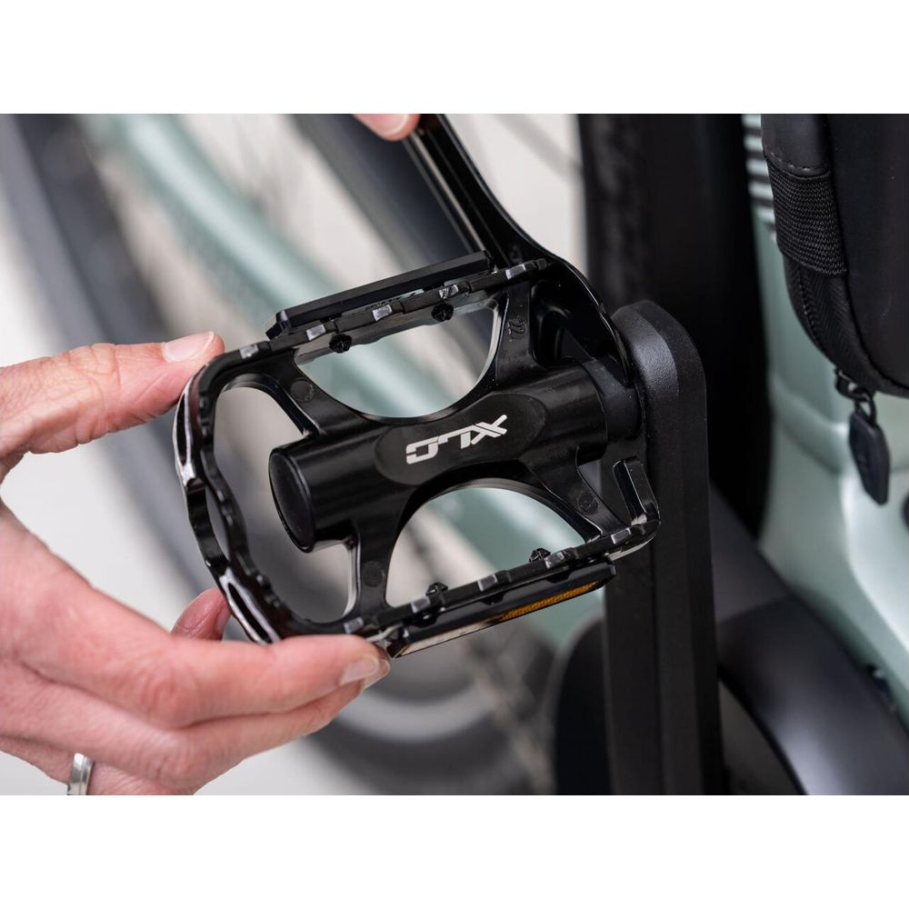 Osoba trzyma czarny pedał rowerowy z logo XLC. Ujęcie z bliska.