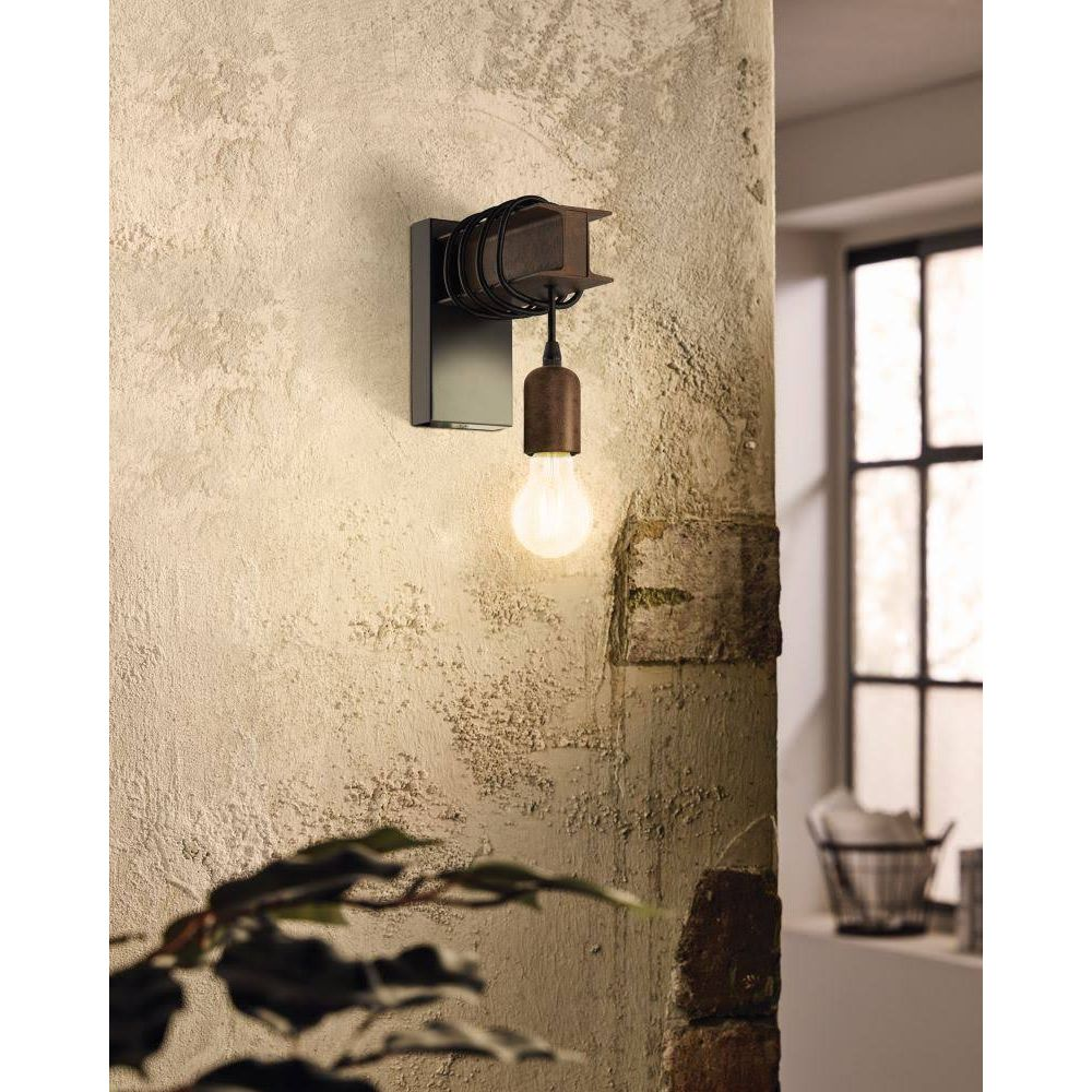 Lámpara de pared industrial con bombilla expuesta y cable negro sobre pared de yeso.
