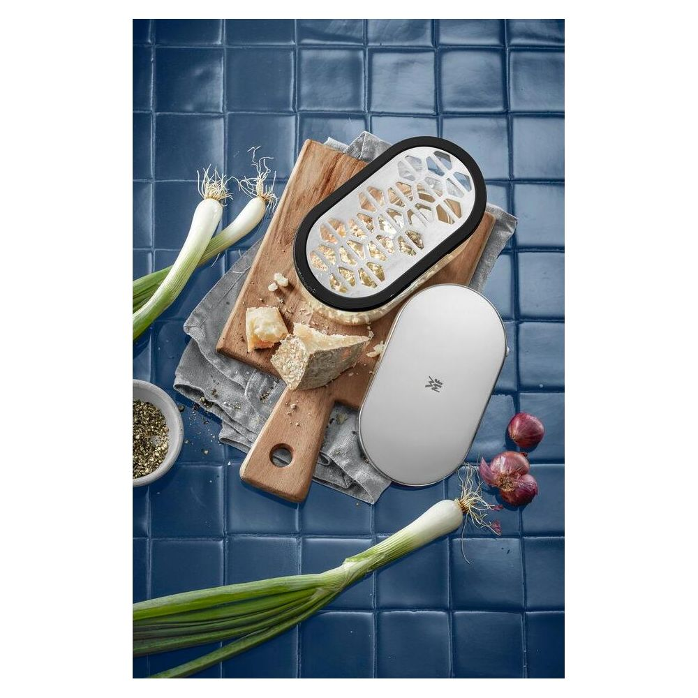 Käse, Zwiebeln, Frühlingszwiebeln, Gewürze und ein Reibe-Set auf blauem Fliesenuntergrund.