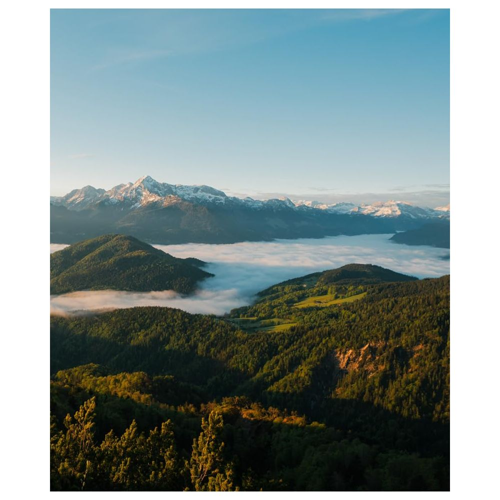 Schneebedeckte Berge über einem Nebelmeer in einem grünen Tal bei Sonnenaufgang.