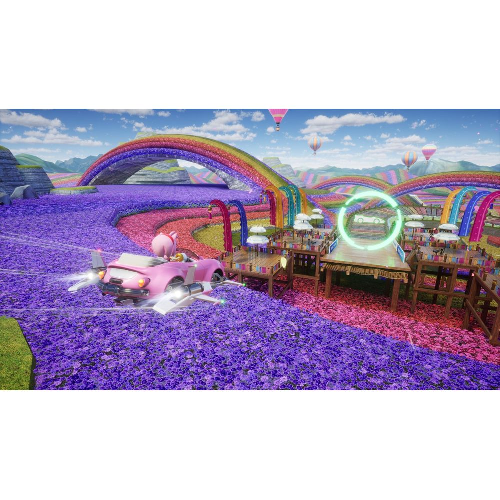 Ein pinkes Auto fährt durch ein Feld aus lila Blumen. Regenbögen und Ballons sind sichtbar.