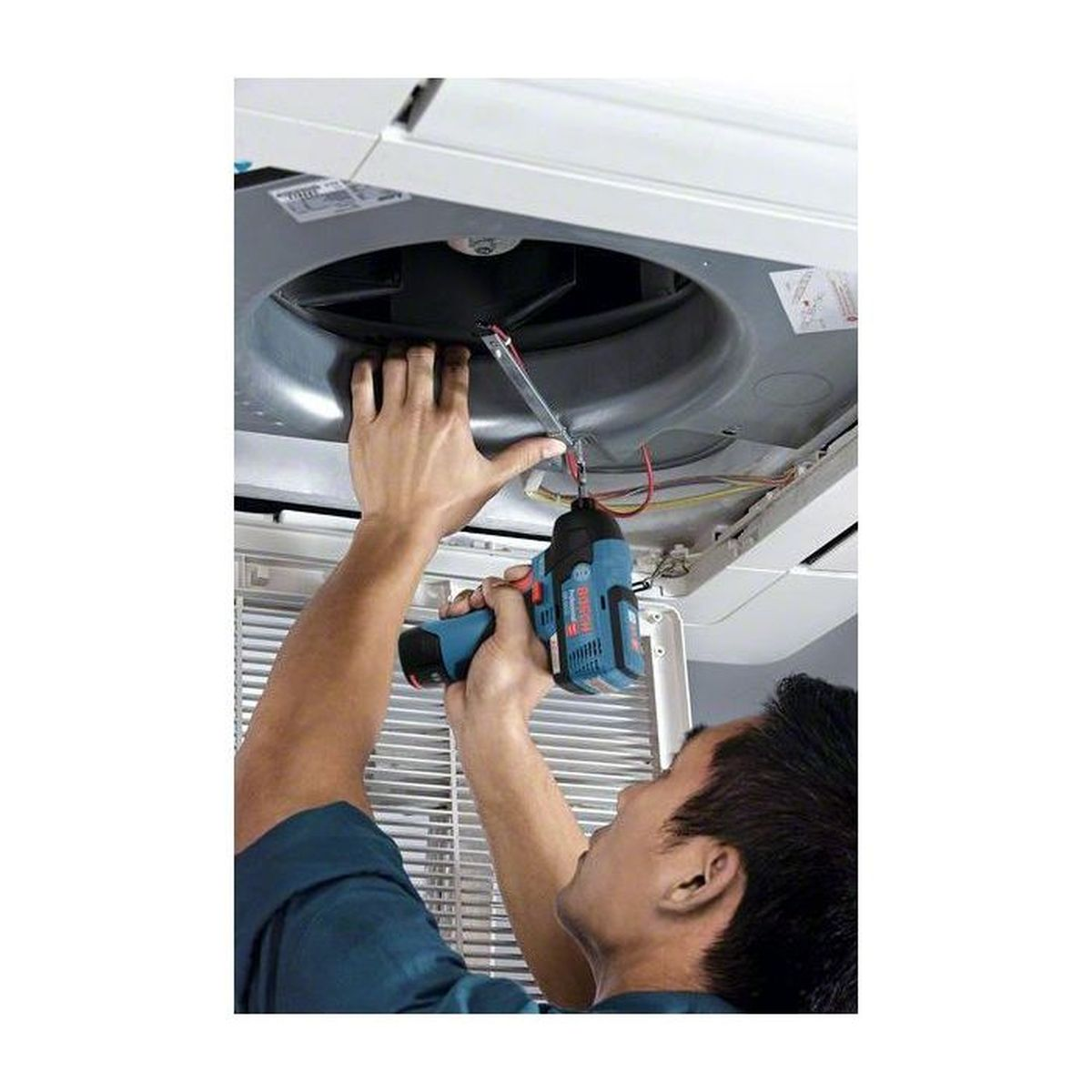 Mężczyzna naprawia klimatyzator niebieskim wiertłem.