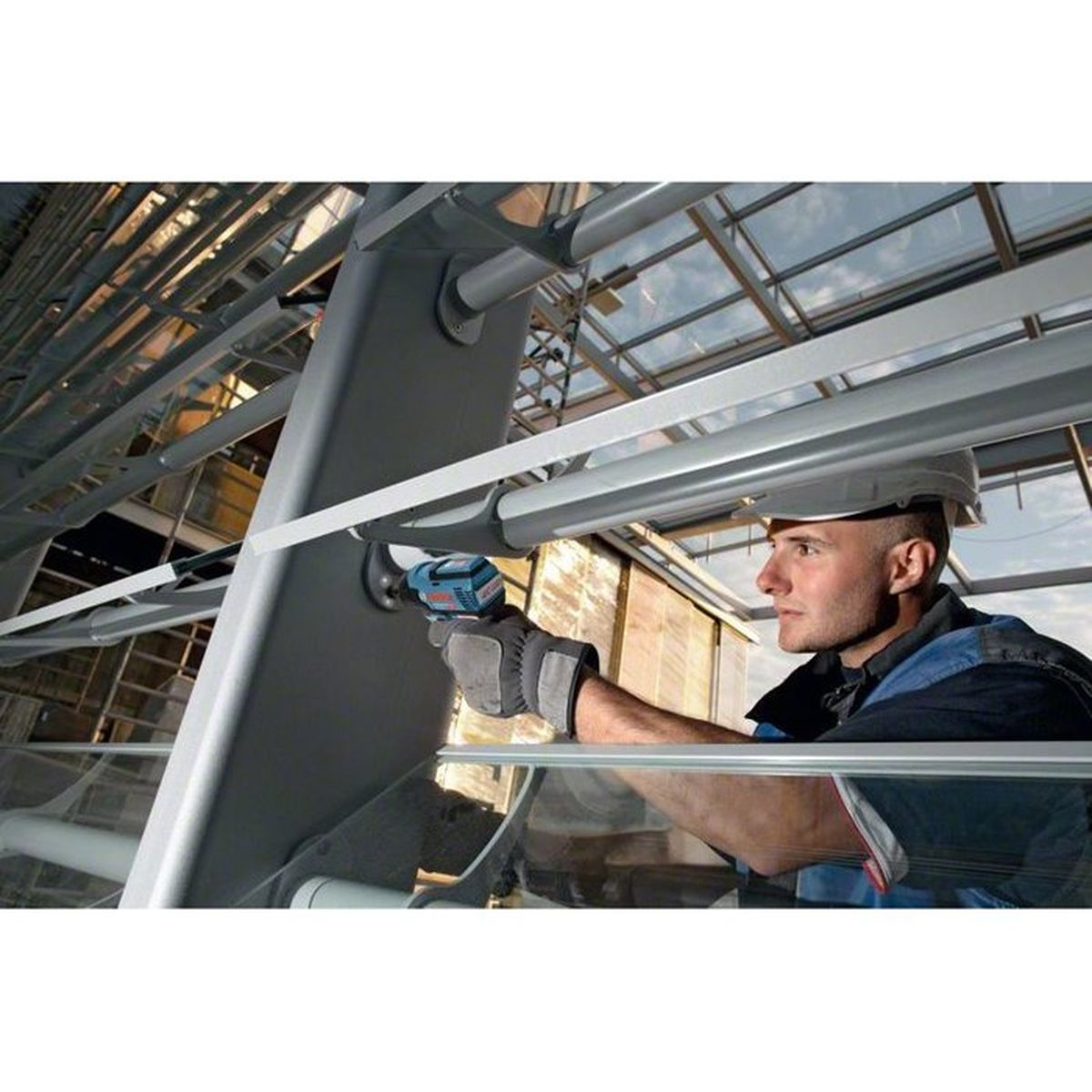 Mężczyzna z wiertarką pracuje przy konstrukcji metalowej.