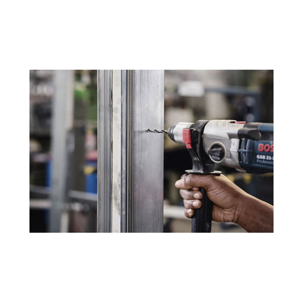 Wiertło wierci dziurę w słupku metalowym. Dłoń trzyma wiertarkę.