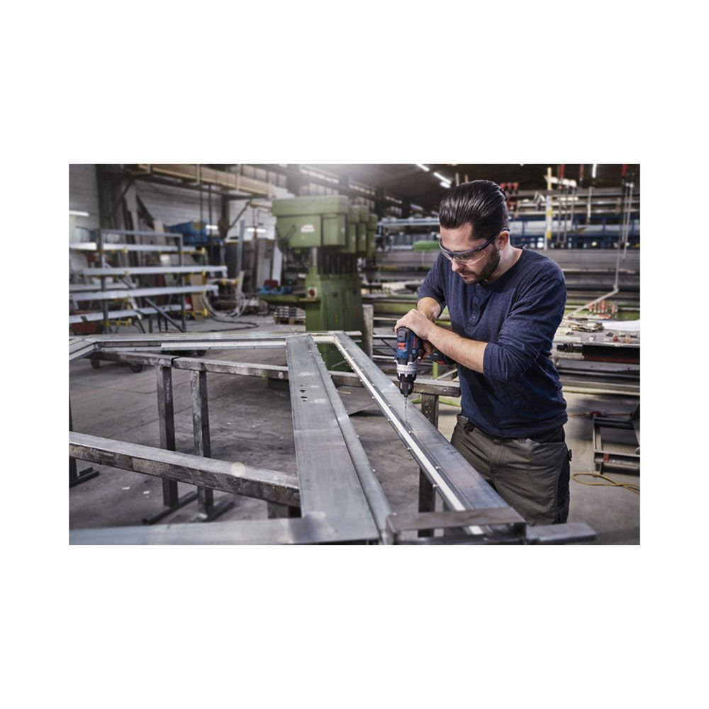 Mężczyzna wierci metalową ramę w warsztacie w okularach ochronnych.