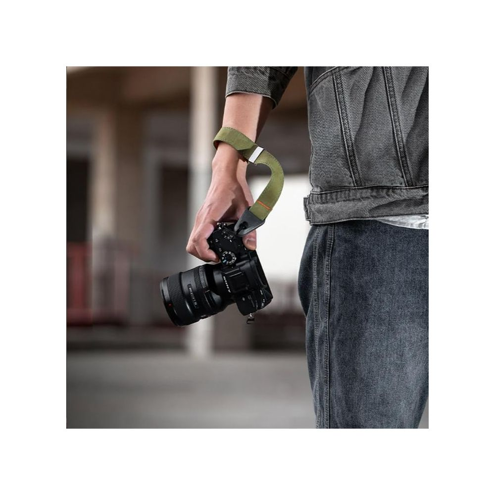 Osoba trzyma czarny aparat z zielonym paskiem. Nosi dżinsową kurtkę.