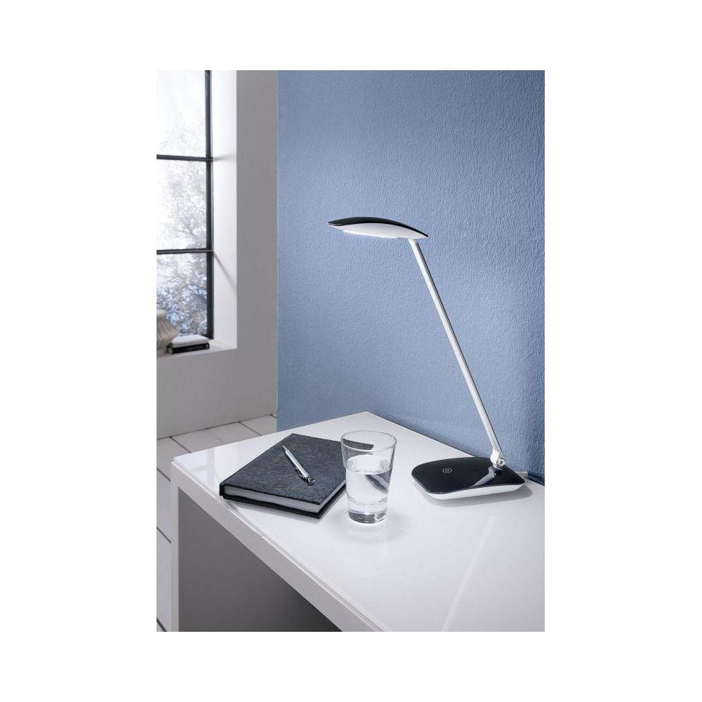 Lampada da scrivania moderna su un tavolo bianco accanto a un taccuino e un bicchiere d'acqua.