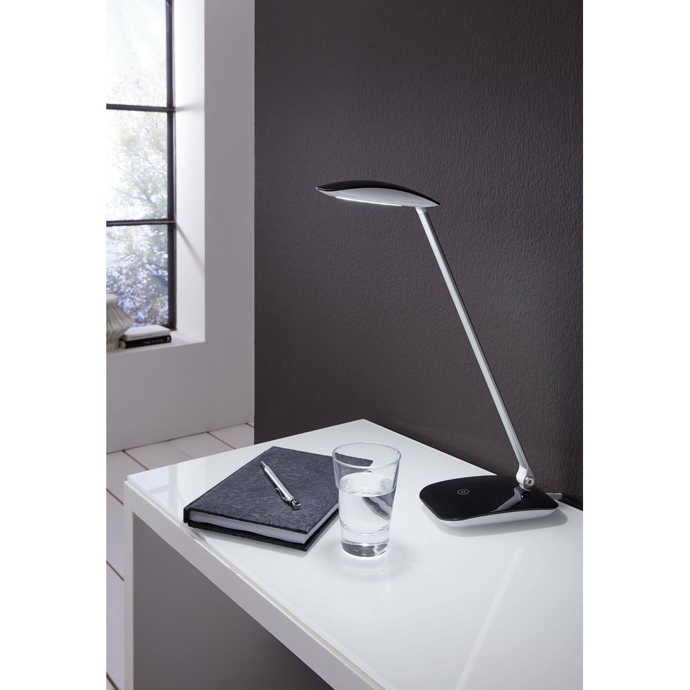 Una scrivania moderna con lampada, taccuino, penna e bicchiere d'acqua.