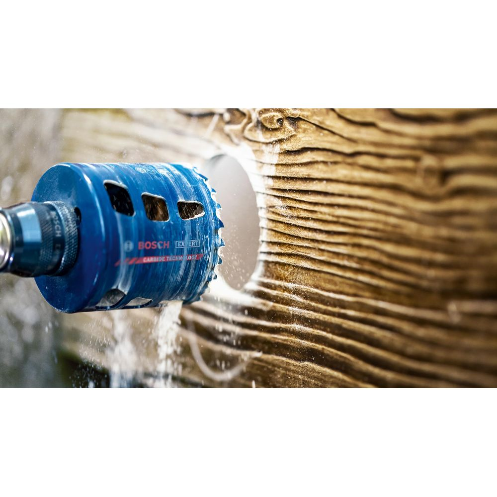 Niebieska otwornica Bosch wierci w drewnie. Lecą iskry.