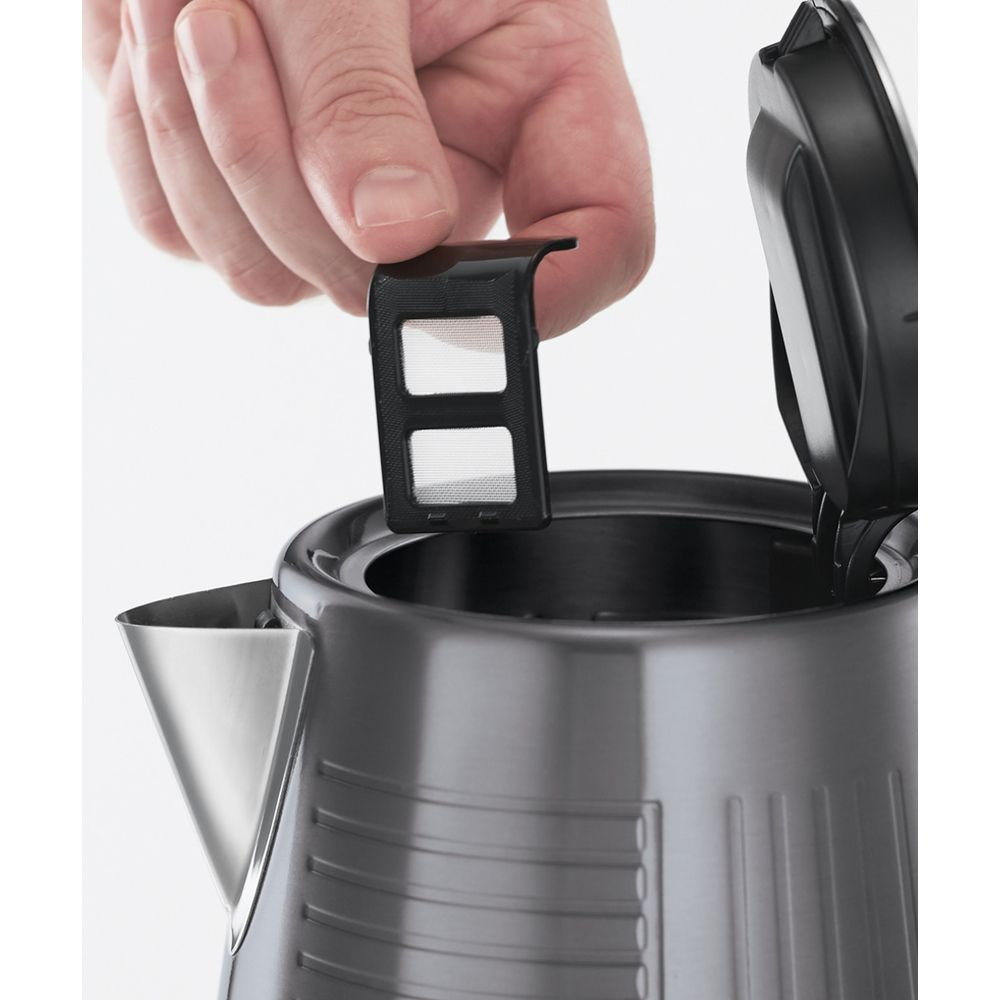 Dłoń trzyma czarny filtr czajnika nad otwartą pokrywą.