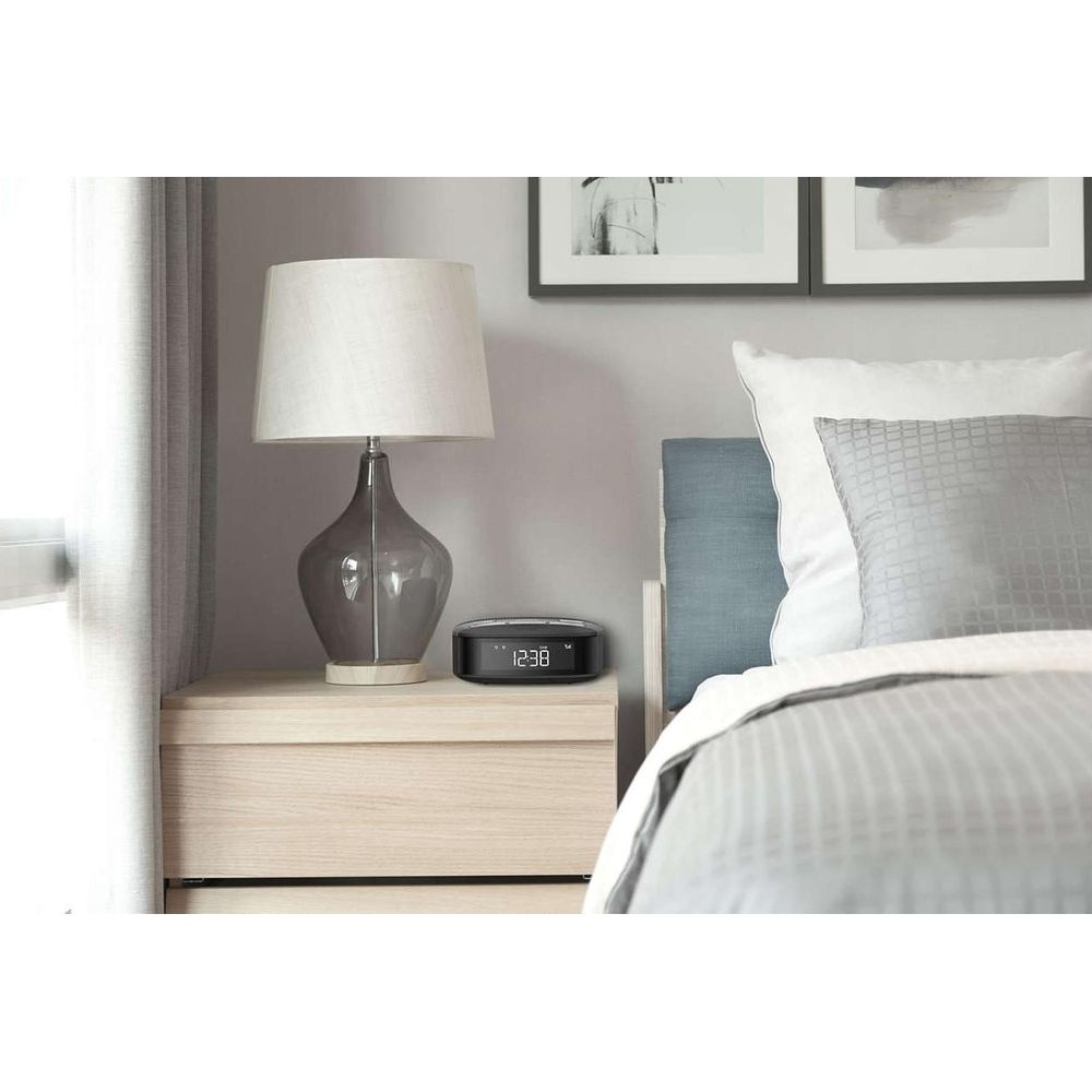 Une table de chevet avec une lampe et un réveil, à côté d'un lit.