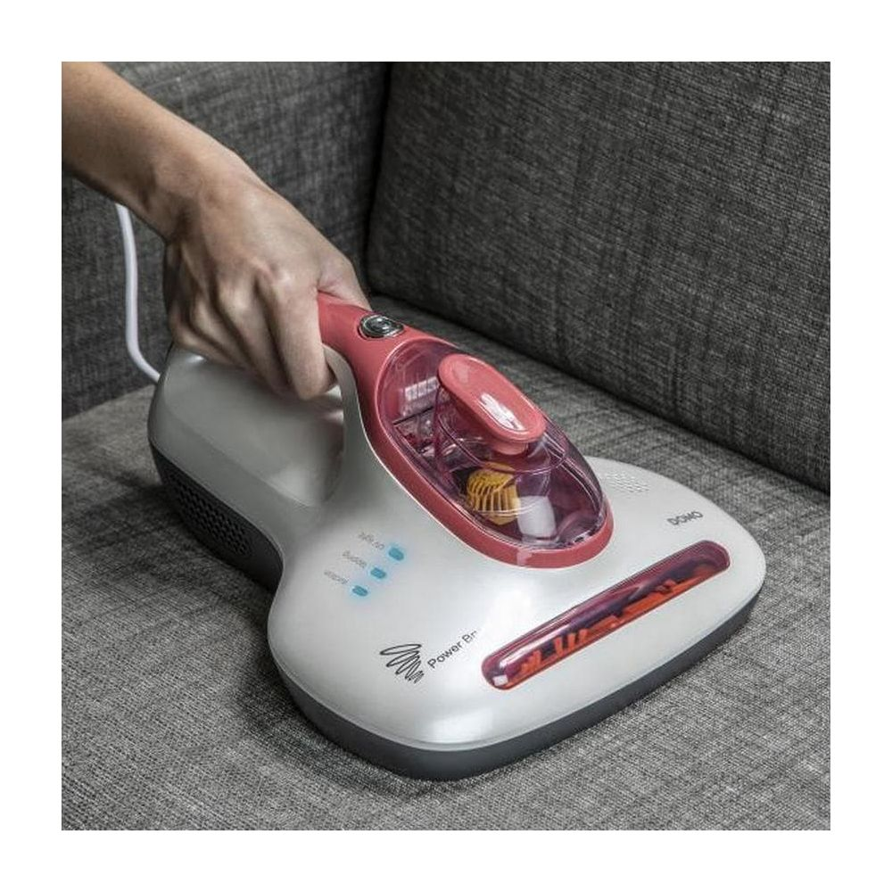 Una mano tiene un aspirapolvere portatile bianco e rosso su un divano grigio.