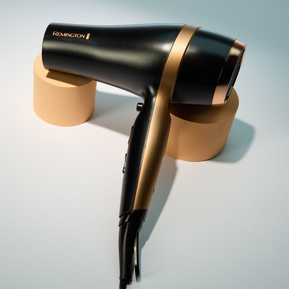Un asciugacapelli Remington nero con accenti dorati poggia su due supporti cilindrici.