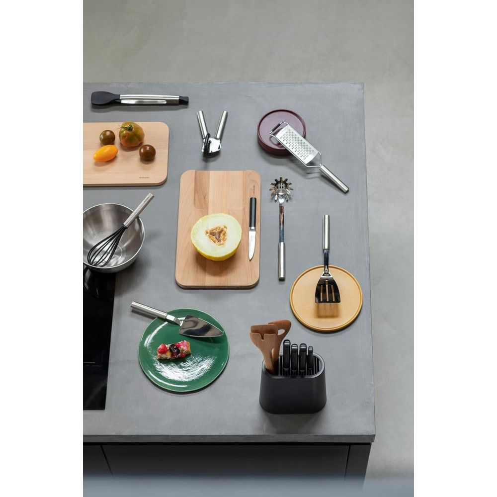 Küchenutensilien: Grater, Löffel, Messer, Schüssel, Schneidebretter, Kuchenstücke.