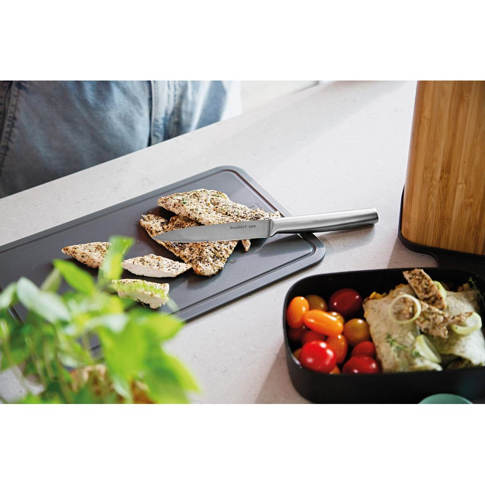 Gekookte kip op een plank met mes, naast tomaten en wrap.