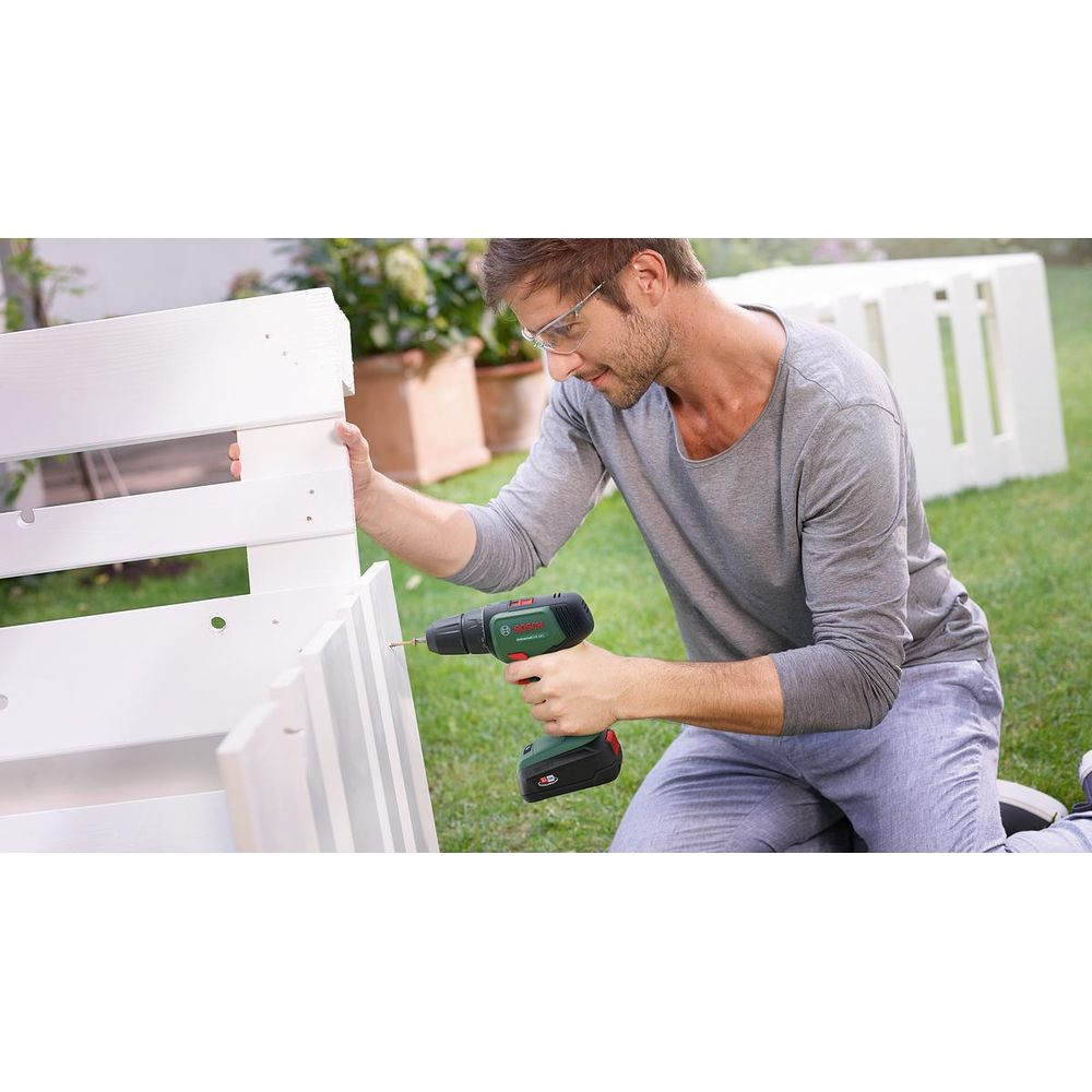 Mężczyzna wierci w białych drewnianych elementach w ogrodzie wkrętarką.